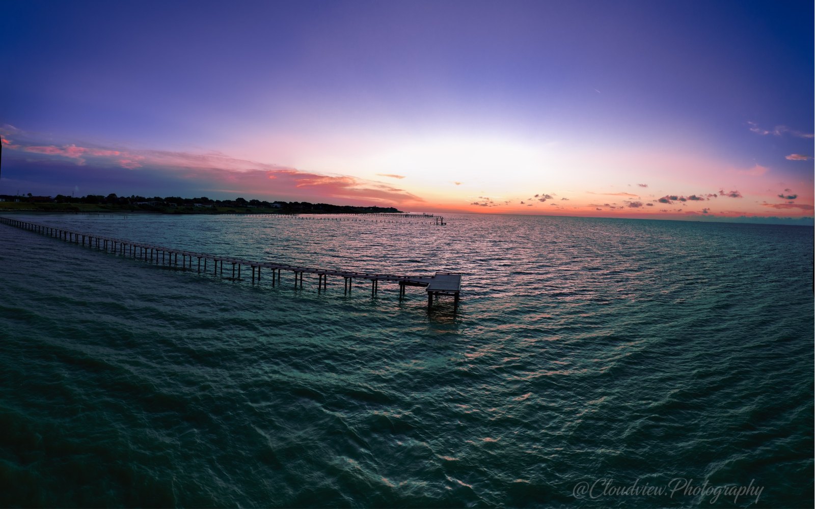 A coastal pier at twilight, purple and teal, dock stretching to horizon.