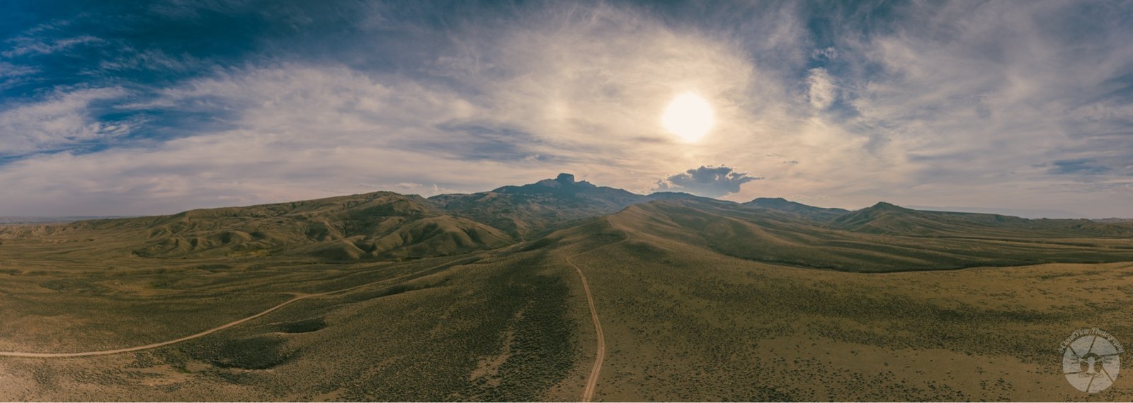 High desert plain with a distant mesa and sun behind clouds.