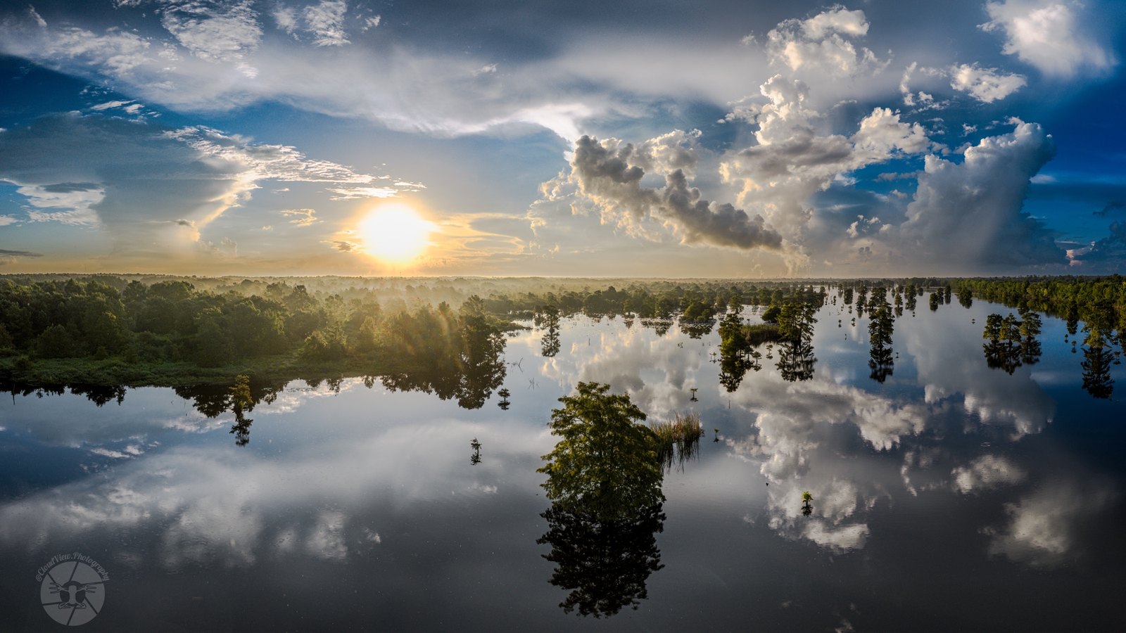 A bayou at sunrise with soft cloud reflections in still water.