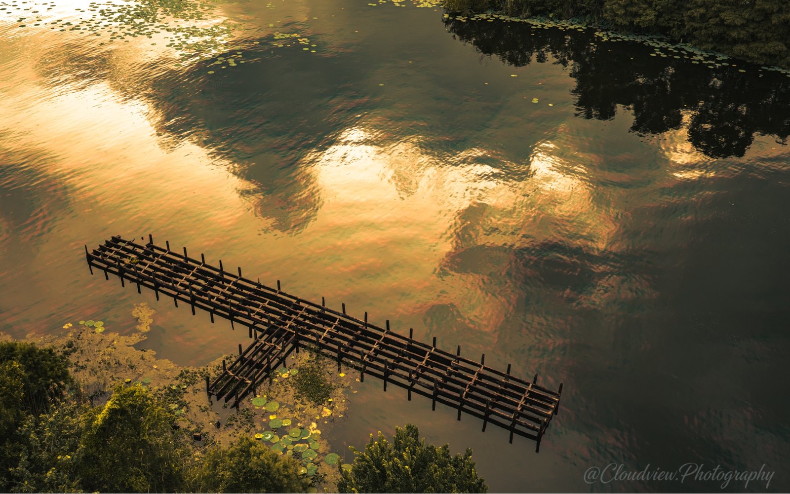 An aerial study of a wooden dock and cloud reflections.